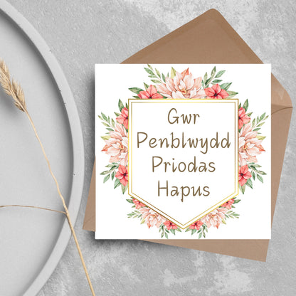 Image of a square wedding anniversary card with &#39;gwr penblwydd priodas hapus&#39; in a subtle handwritten style font, which translates to &#39;happy wedding anniversary&#39; in welsh. the text is against a white banner surrounded by pink flowers