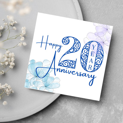 Square Card with white background, there are blue faded watercolour flowers on each corner and dark blue text reads &#39;Happy 20 year anniversary&#39; the words are in a script font and the number is an ornate filigree style