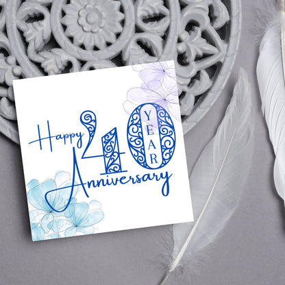 Square Card with white background, there are blue faded watercolour flowers on each corner and dark blue text reads &#39;Happy 40 year anniversary&#39; the words are in a script font and the number is an ornate filigree style