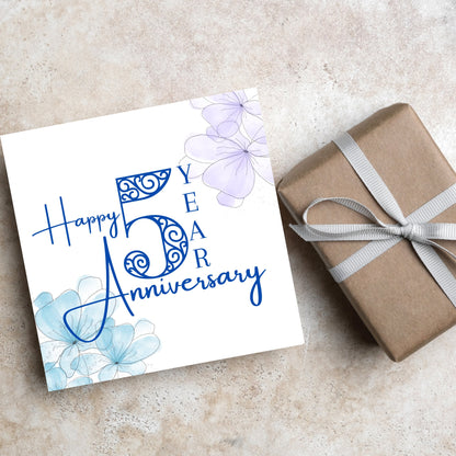 Square Card with white background, there are blue faded watercolour flowers on each corner and dark blue text reads &#39;Happy 5 year anniversary&#39; the words are in a script font and the number is an ornate filigree style