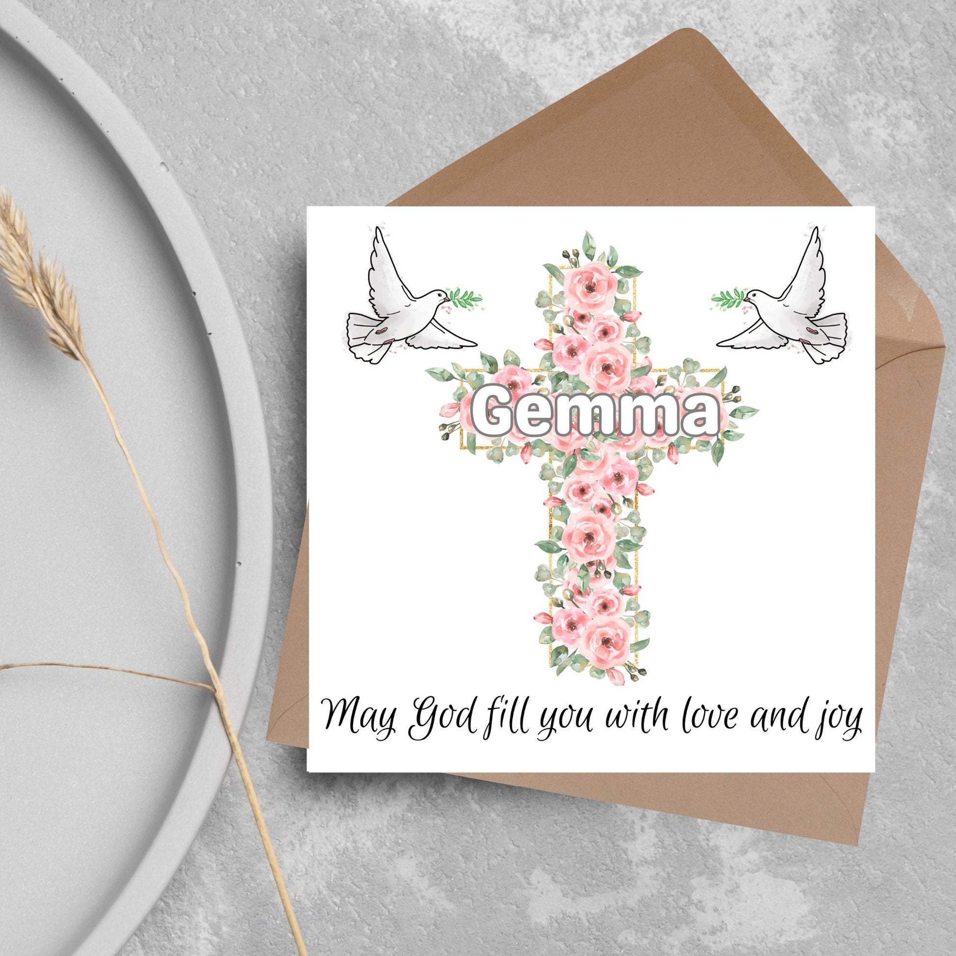 Square white card with a cross made of pink roses at the centre with the chosen name written across in white. either side of the cross is a white dove flying. At the bottom the text &#39;may god fill you with love and joy&#39; is written