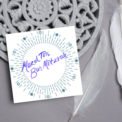 square bar mitzvah card with a white background and the text &#39;mazel tav, bar mitzvah&#39; in the centre in a blue handwritten script style font. Surrounding the text is a circle made of concentric blue lines and 12 stars of david