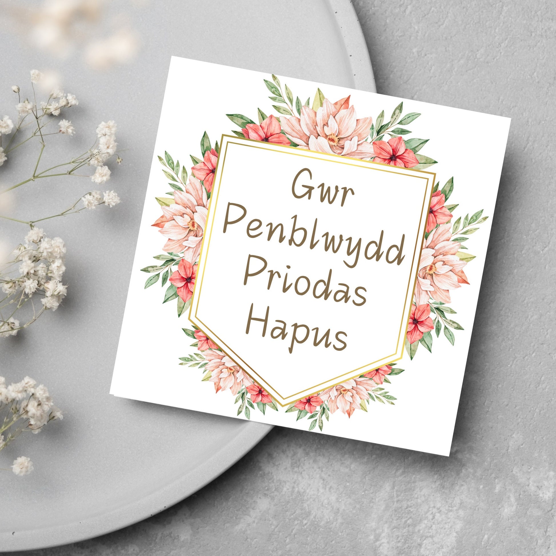 Image of a square wedding anniversary card with &#39;gwr penblwydd priodas hapus&#39; in a subtle handwritten style font, which translates to &#39;happy wedding anniversary&#39; in welsh. the text is against a white banner surrounded by pink flowers