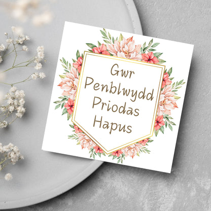 Image of a square wedding anniversary card with &#39;gwr penblwydd priodas hapus&#39; in a subtle handwritten style font, which translates to &#39;happy wedding anniversary&#39; in welsh. the text is against a white banner surrounded by pink flowers