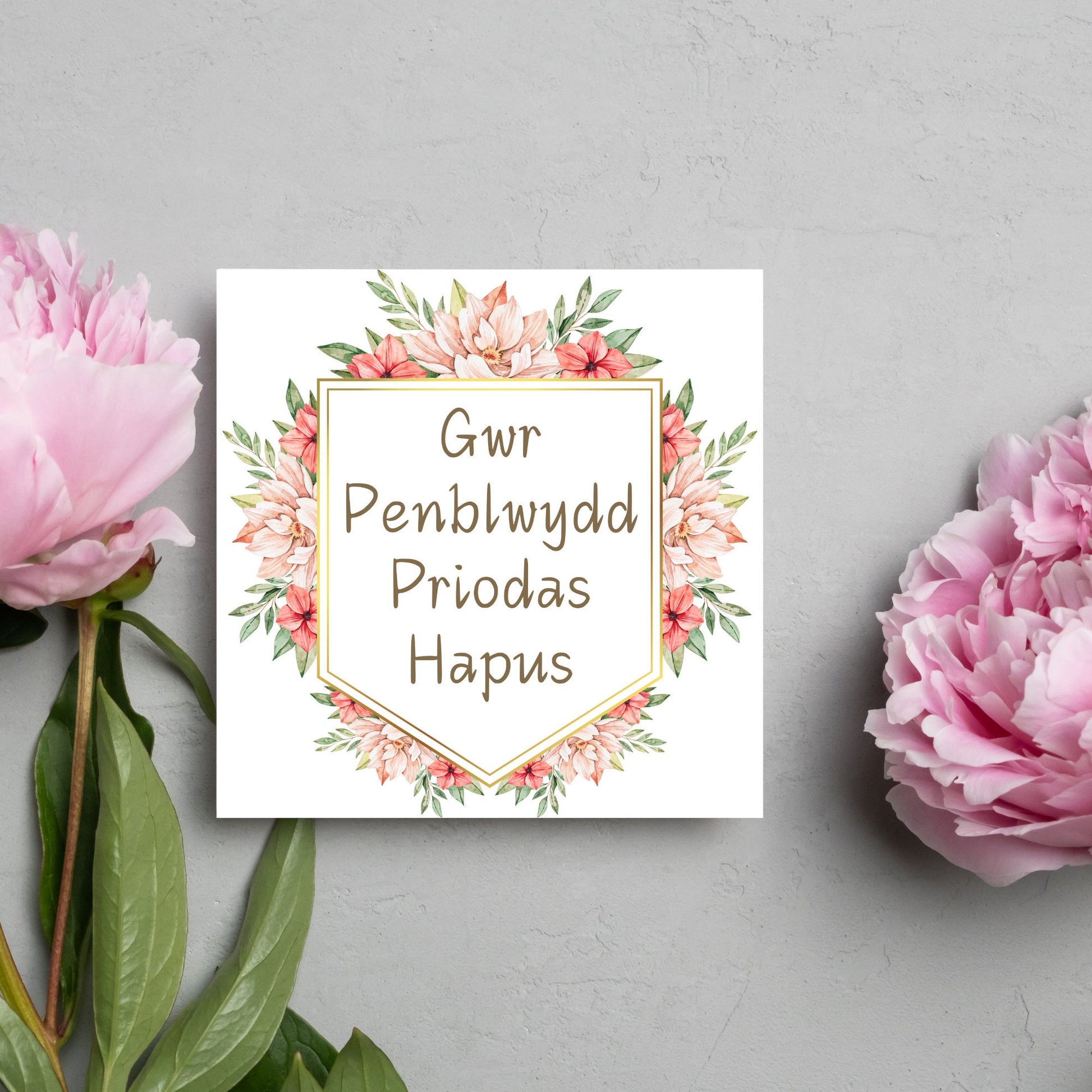 Image of a square wedding anniversary card with &#39;gwr penblwydd priodas hapus&#39; in a subtle handwritten style font, which translates to &#39;happy wedding anniversary&#39; in welsh. the text is against a white banner surrounded by pink flowers