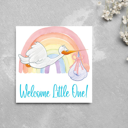 square new baby card with a flying cartoon stork delivering a swaddled baby against a watercolour rainbow in pastel shades. A cursive style text reads &#39;welcome little one&#39; in a light blue font at the bottom of the card