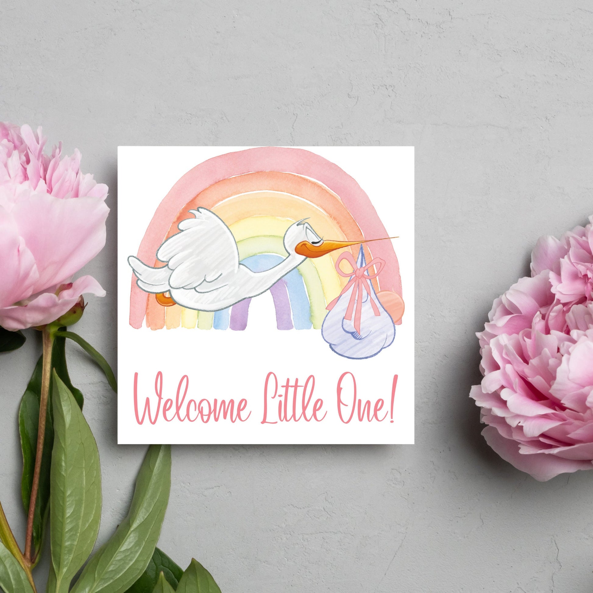 square new baby card with a flying cartoon stork delivering a swaddled baby against a watercolour rainbow in pastel shades. A cursive style text reads &#39;welcome little one&#39; in a light pink font at the bottom of the card