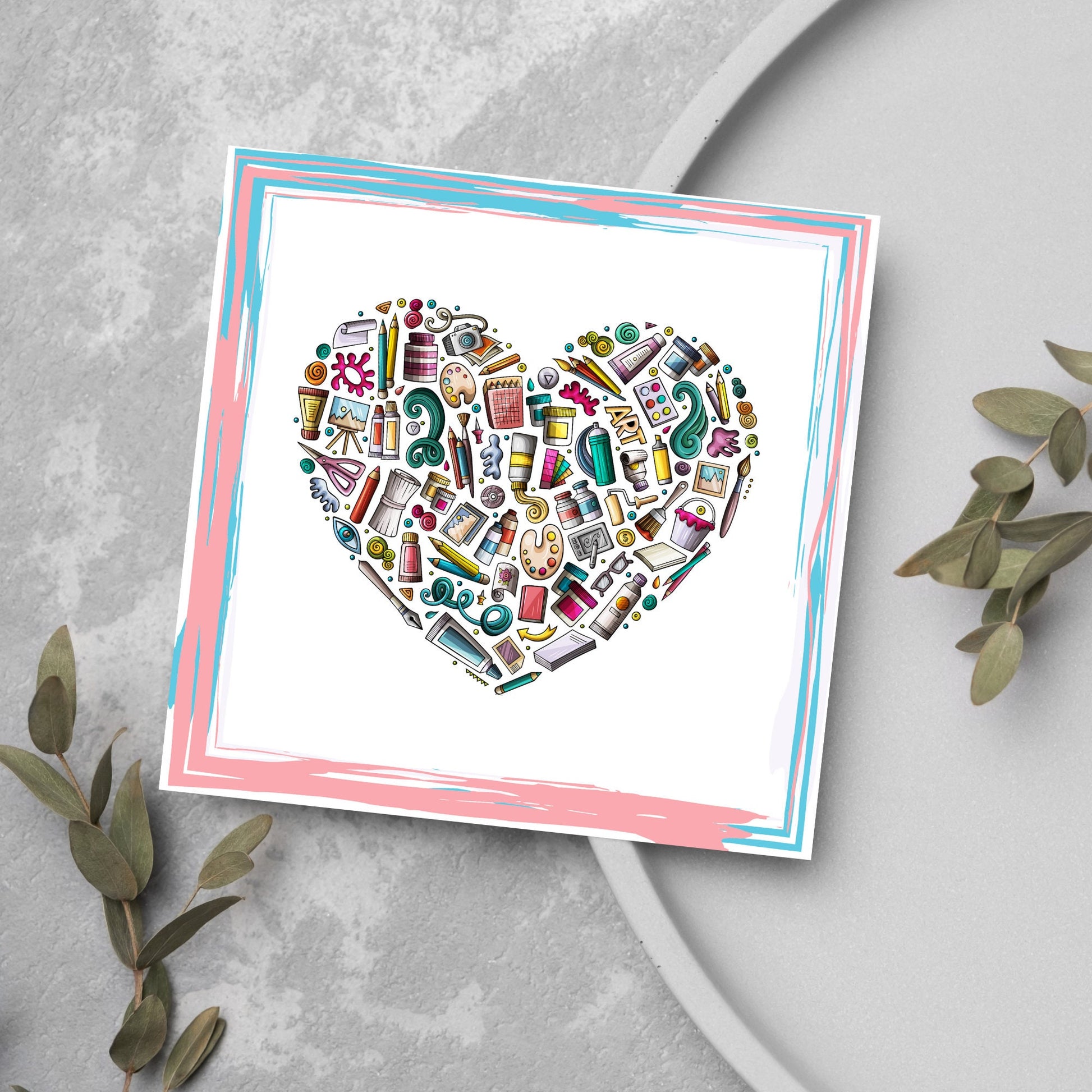 Image of a square greetings card against a grey background. The design is a heart made up of artist supplies