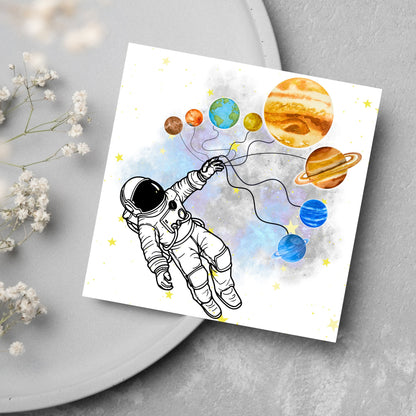 This square shaped card has an illustration of an astronauts holding the planets of the milky way in a watercolour inspired design. There is a collection of yellow stars and a watercolour nebula in the background