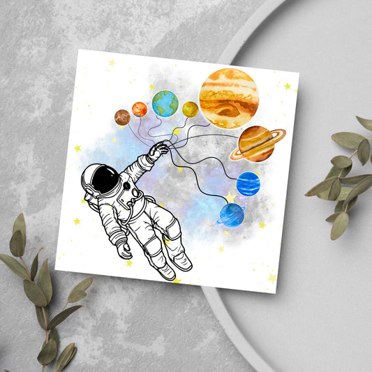 This square shaped card has an illustration of an astronauts holding the planets of the milky way in a watercolour inspired design. There is a collection of yellow stars and a watercolour nebula in the background