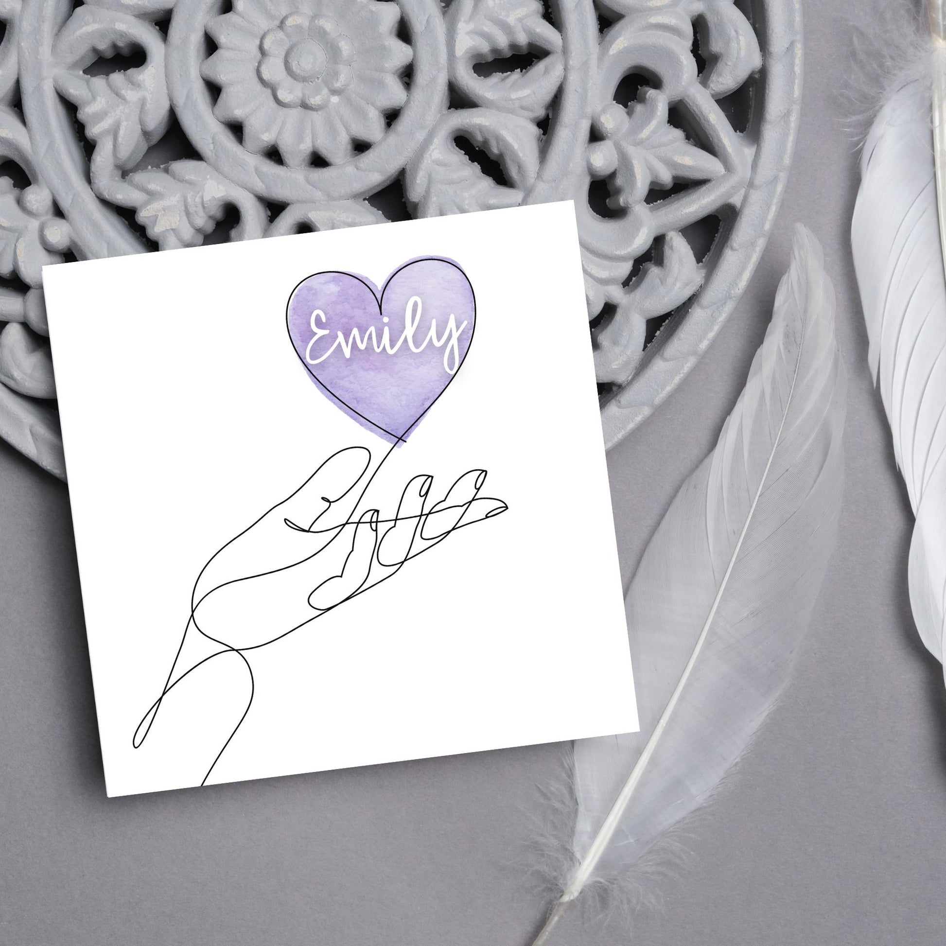 square card with a simple black and white one line drawing of an open hand with a heart rising from the hand. the heart has a purple background and has a personalised name written in a white cursive text