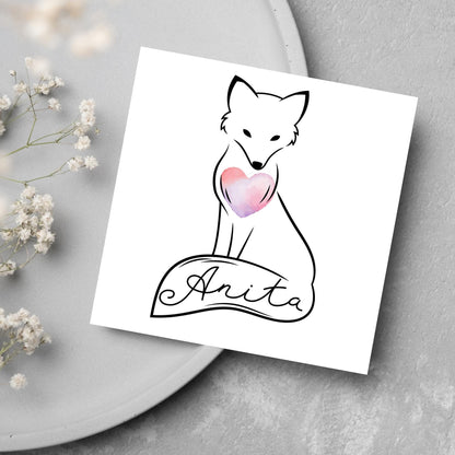 Square card with simple black line drawing of a fox  sitting with its tail wrapped around its feet. It has a pink watercolour heart on its chest and personalised with a name on the tail in a calligraphy font