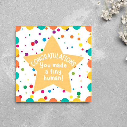 Image of a square card, the card design is a multicoloured polka dot design with a large yellow coloured star in the middle and white text against the star that reads CONGRATULATIONS You made a tiny human!