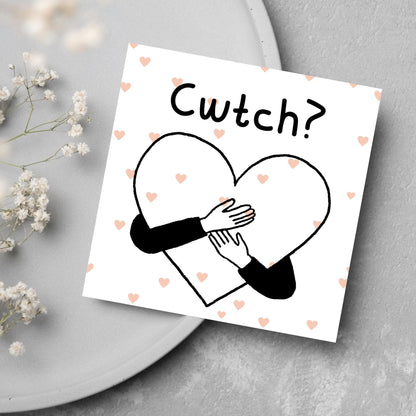 Square Greeting card small with subtle pink hearts in the background of a line drawn heart with hands hugging it and the word CWTCH? above it in handwritten style text