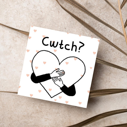 Square Greeting card small with subtle pink hearts in the background of a line drawn heart with hands hugging it and the word CWTCH? above it in handwritten style text
