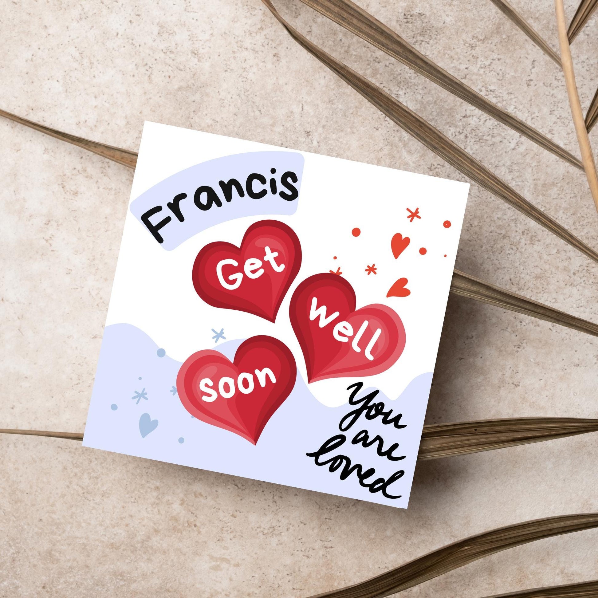 square card with white and blue background. 3 red hearts are in the centre of the card with get well soon overlayed in white, the top corner has curved text with the recipients name and in the bottom corner the text you are loved in black cursive