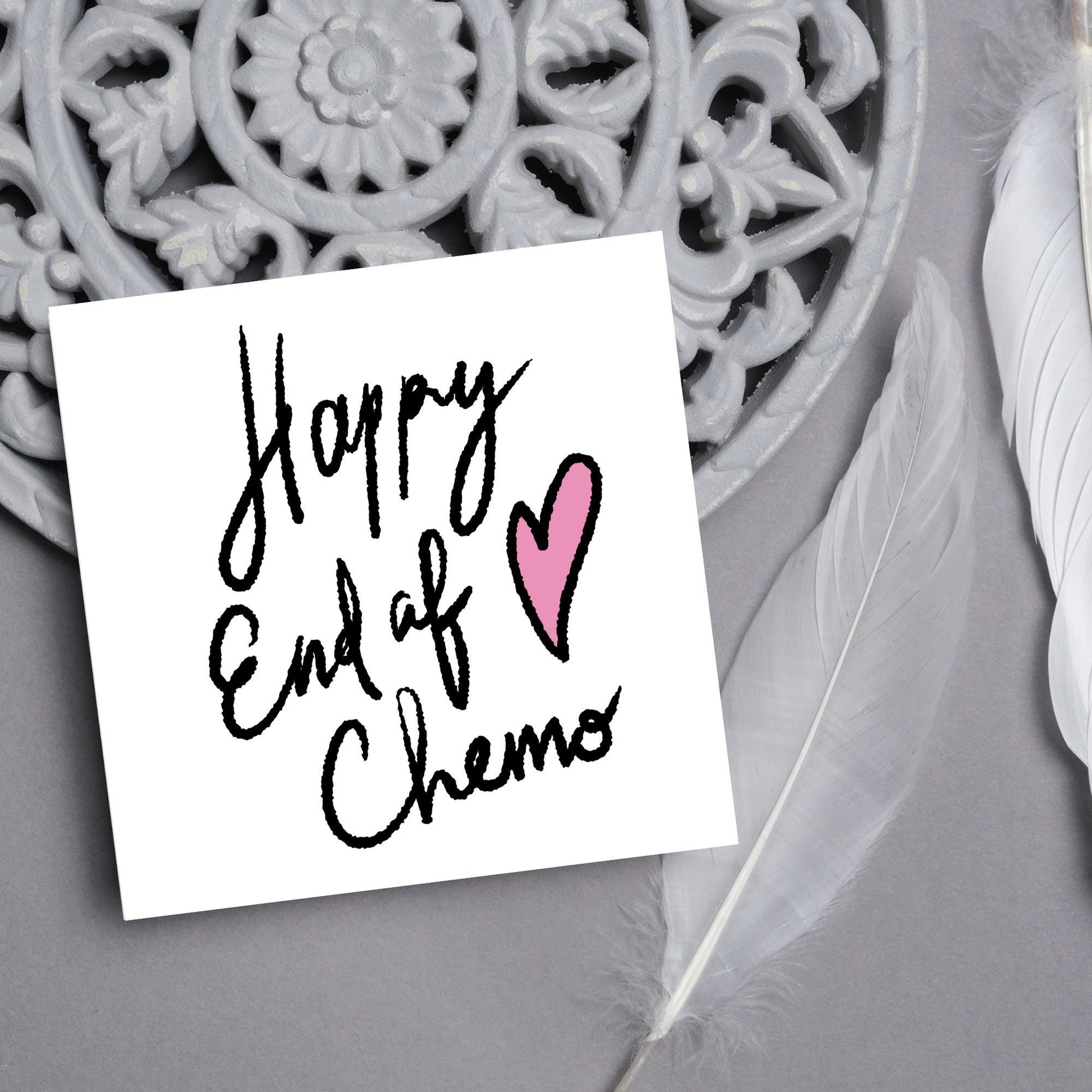Simple square card with a white backdrop and black handwritten style text that reads HAPPY END OF CHEMO with a roughly drawn pink heart next to the text.