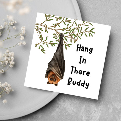 square card with an illustration of a bat hanging upside down from a tree branch with black text next to it that reads - Hang in there buddy