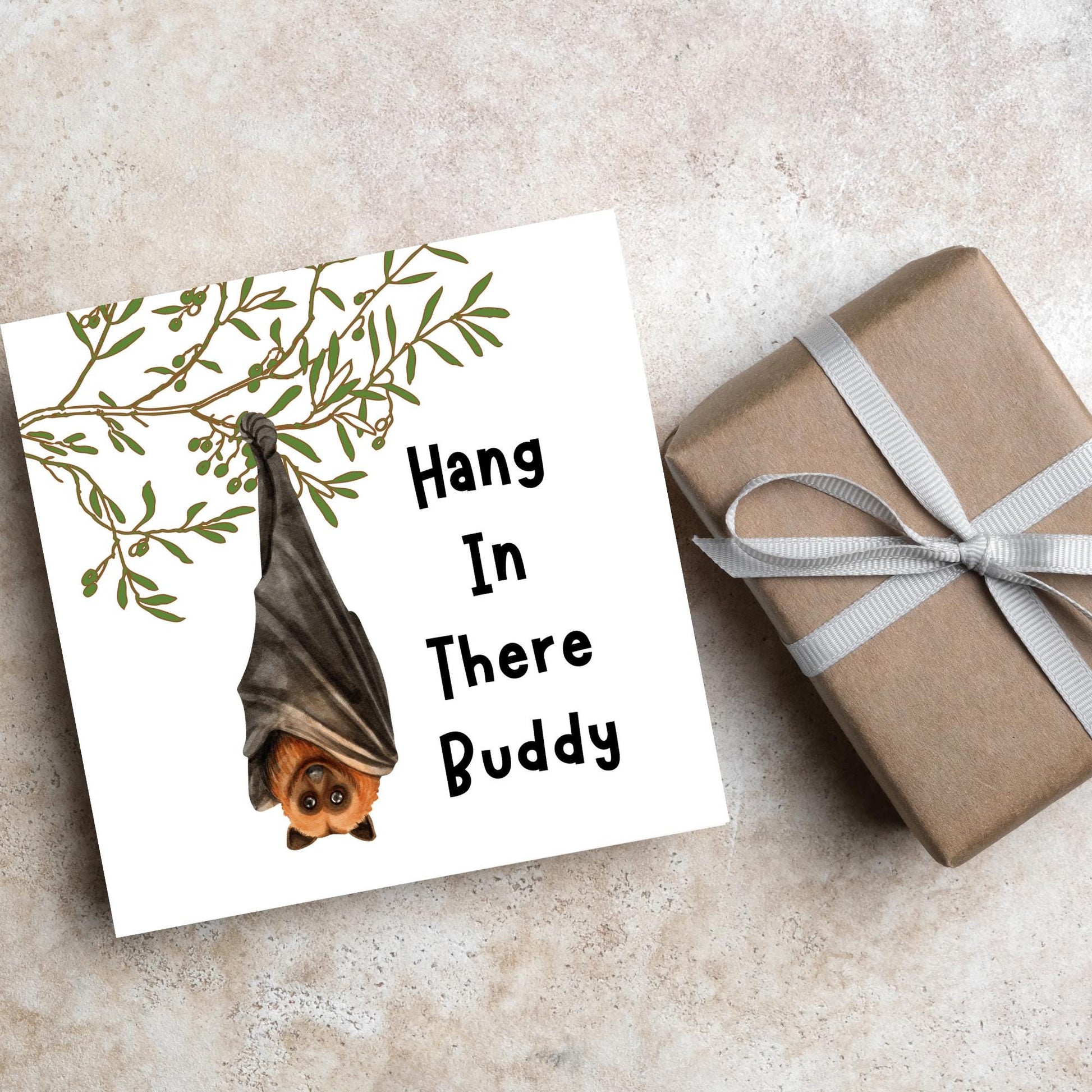 square card with an illustration of a bat hanging upside down from a tree branch with black text next to it that reads - Hang in there buddy