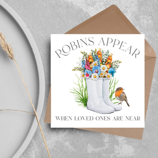 Square card with a watercolour image of a robin sitting on a pair of wellington boots that at filled with flowers. Elegant text reads Robins Appear when loved ones are near
