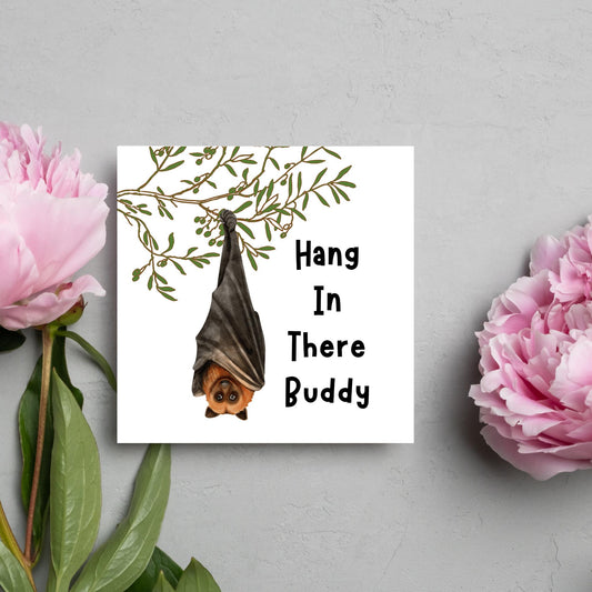 square card with an illustration of a bat hanging upside down from a tree branch with black text next to it that reads - Hang in there buddy