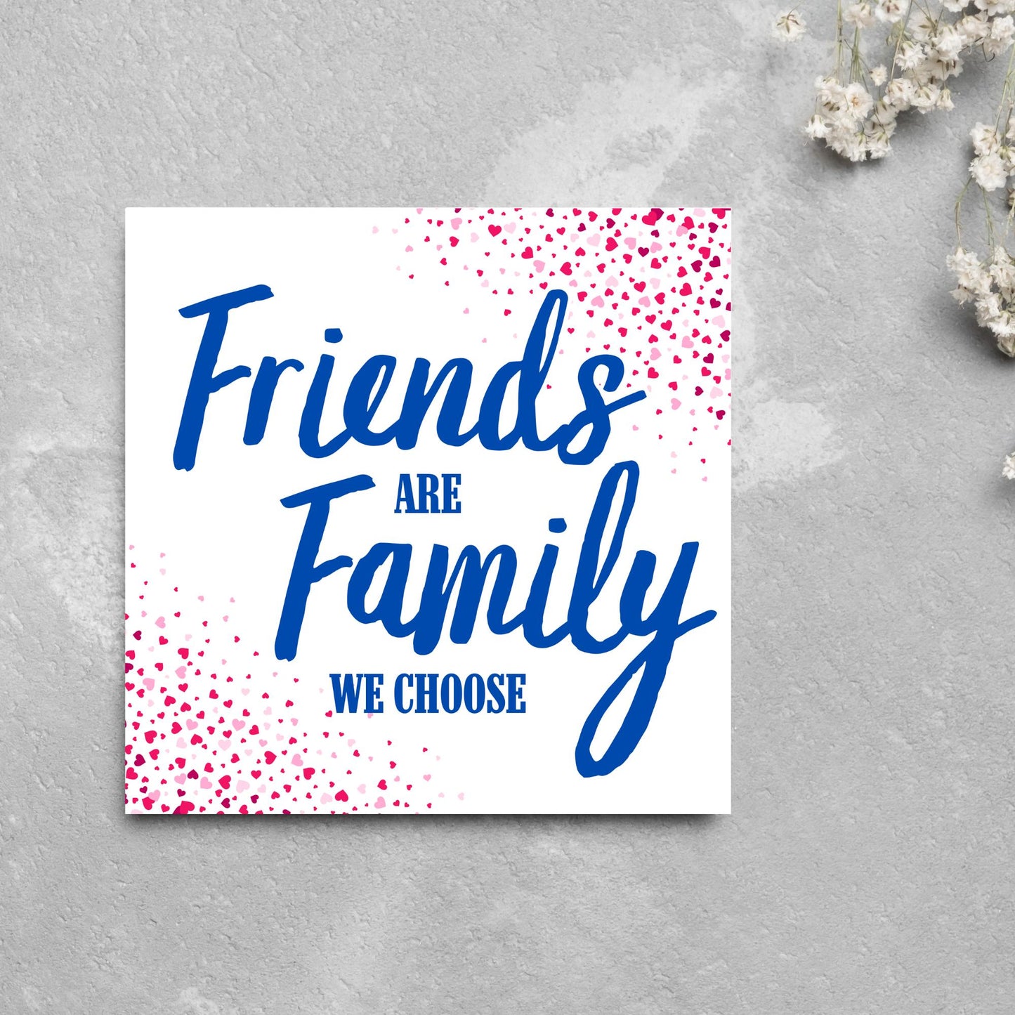 Square card with small hearts on opposite corners in shades of pink and blue writing in the centre that reads Friends are Family we choose