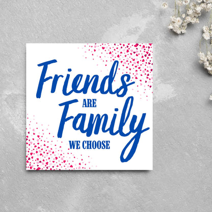 Square card with small hearts on opposite corners in shades of pink and blue writing in the centre that reads Friends are Family we choose