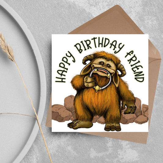 This square shaped card has an illustration of Ludo from the 80s Bowie film Labyrinth. Ludo towers over some rocks and has a door knocker in their mouth. The caption reads Happy Birthday Friend, this text arches above Ludo. This card is perfect for any fans of the film Labyrinth