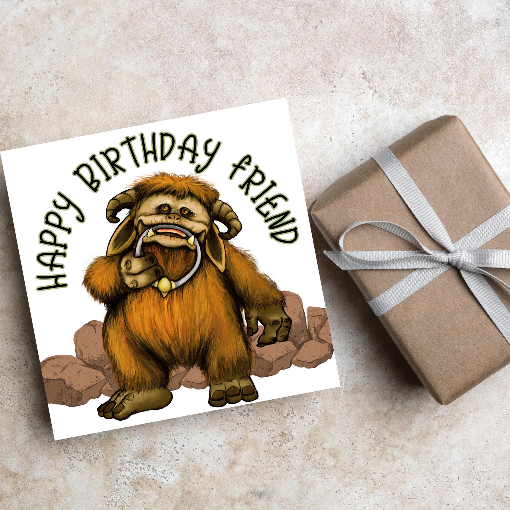 This square shaped card has an illustration of Ludo from the 80s Bowie film Labyrinth. Ludo towers over some rocks and has a door knocker in their mouth. The caption reads Happy Birthday Friend, this text arches above Ludo. This card is perfect for any fans of the film Labyrinth