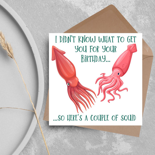 Image of a square birthday card. The background of the card is white and there is an illustration of 2 red squid in the centre. Writing surrounds the picture with &#39;I didn&#39;t know what to get you for your birthday....so here&#39;s a couple of squid&#39; in a green capitalised handwritten font.