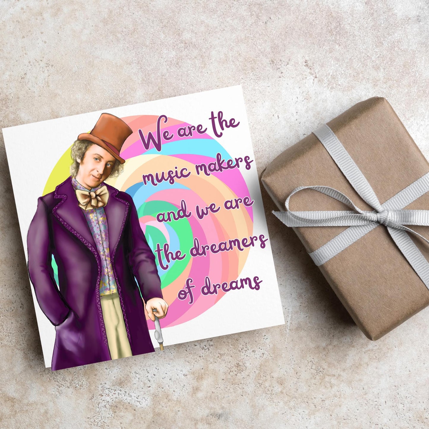 Image of a square greeting card. The background of the card is white and there is a hand drawn image of Gene Wilder as Willy Wonka wearing his purple coat, top hat and bow tie. Behind him is a colourful swirly lollypop and purple text reads &#39;we are the music makers and we are the dreamers of dreams&#39; in a curly font.