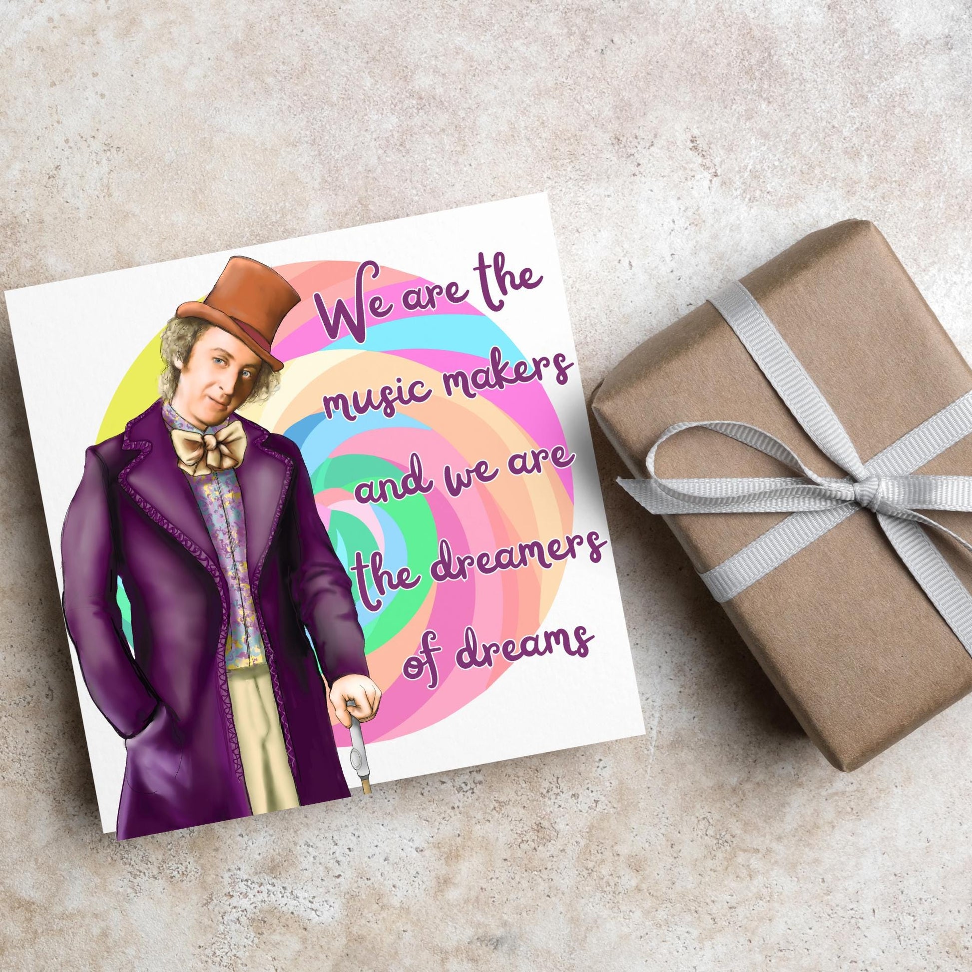 Image of a square greeting card. The background of the card is white and there is a hand drawn image of Gene Wilder as Willy Wonka wearing his purple coat, top hat and bow tie. Behind him is a colourful swirly lollypop and purple text reads &#39;we are the music makers and we are the dreamers of dreams&#39; in a curly font.