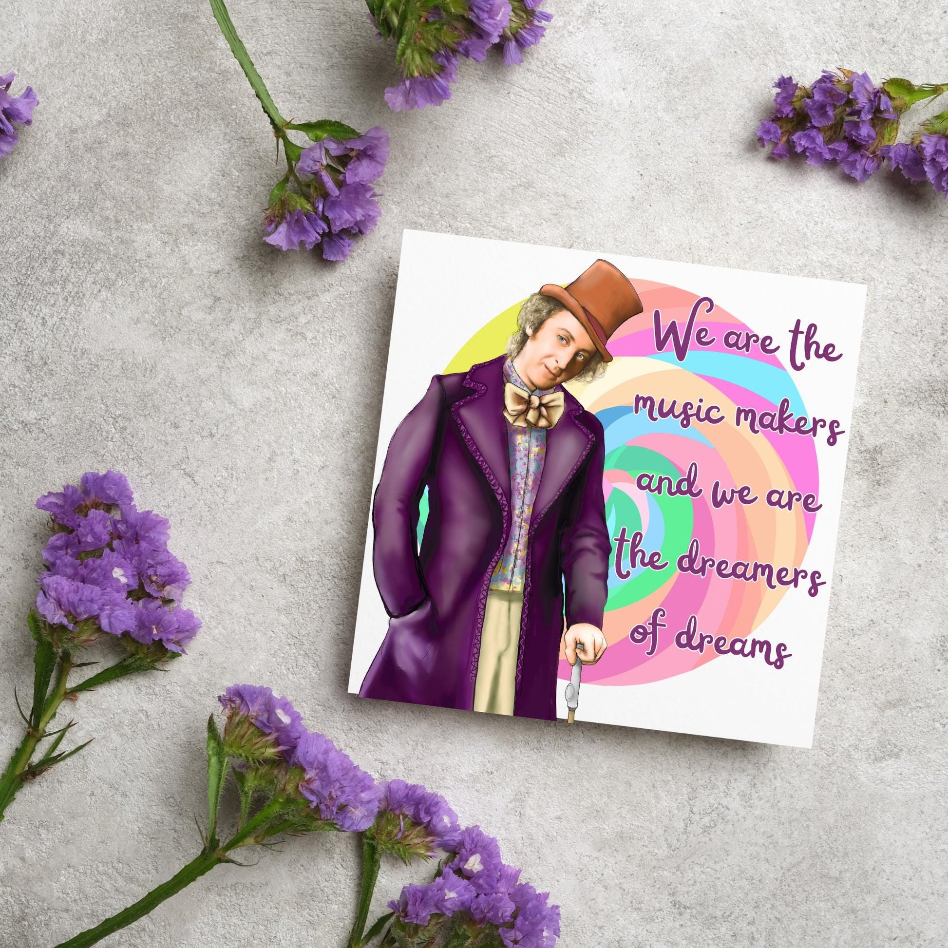 Image of a square greeting card. The background of the card is white and there is a hand drawn image of Gene Wilder as Willy Wonka wearing his purple coat, top hat and bow tie. Behind him is a colourful swirly lollypop and purple text reads &#39;we are the music makers and we are the dreamers of dreams&#39; in a curly font.
