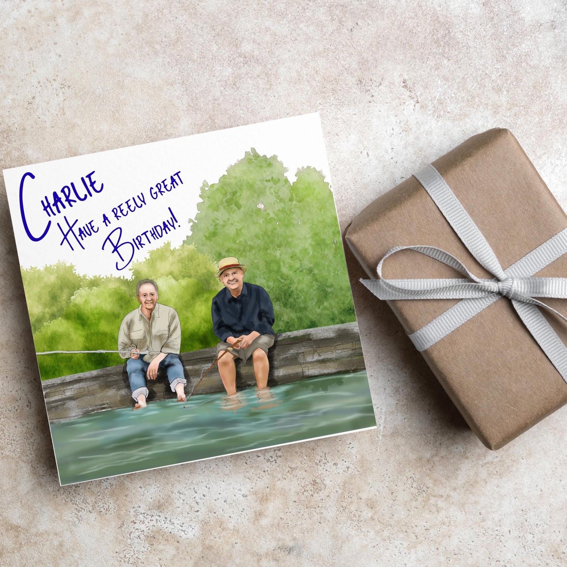 square greetings card with a hand drawn image of bob Mortimer and paul Whitehouse sitting on the edge of a dock fishing with their bare feet in the water. behind them are watercolour trees and bushes and blue text that reads &#39;charlie, have a freely great birthday&#39; in a handwritten style font